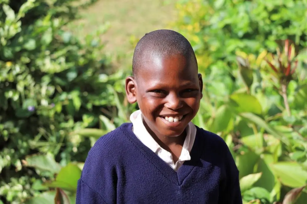 A young boy smiling for the camera in front of some bushes.