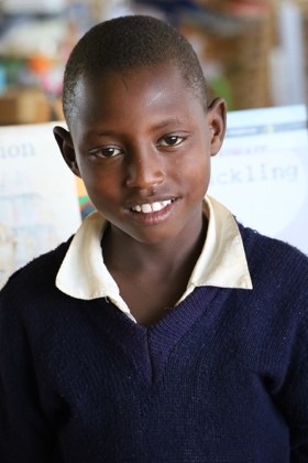 A young boy in school uniform smiling for the camera.