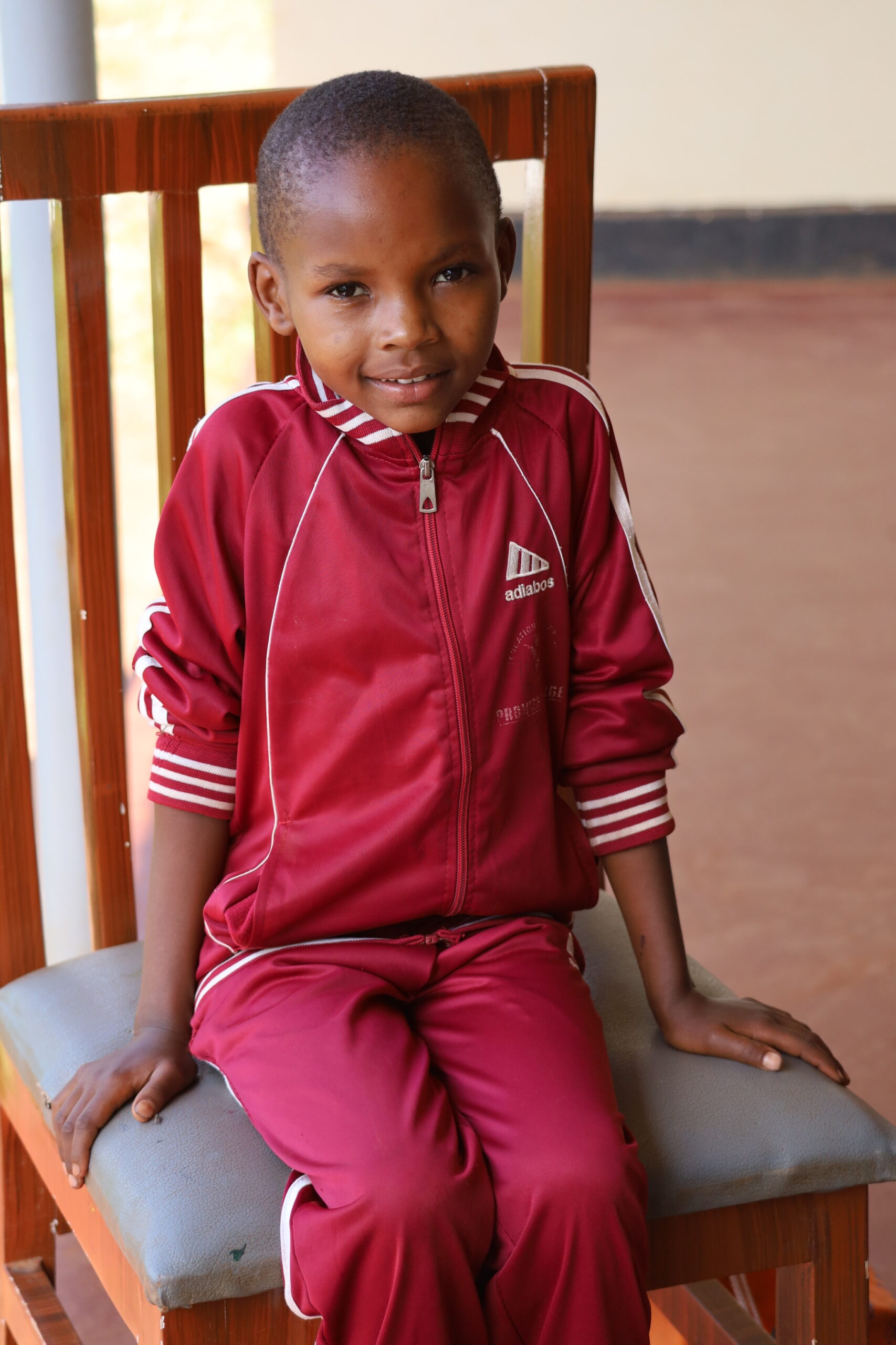 A young boy in red and white jacket sitting on chair.